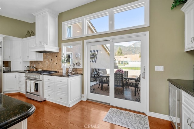 kitchen with light wood finished floors, premium range hood, high end stainless steel range oven, and white cabinets