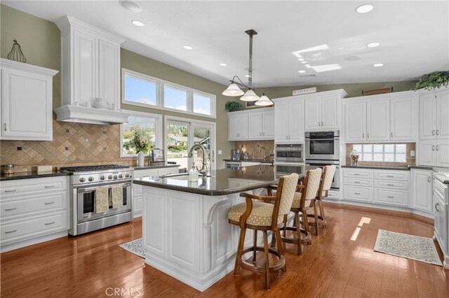 kitchen with pendant lighting, a center island with sink, appliances with stainless steel finishes, a sink, and a kitchen breakfast bar