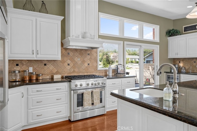 kitchen with dark stone counters, white cabinets, high end stainless steel range oven, and a sink