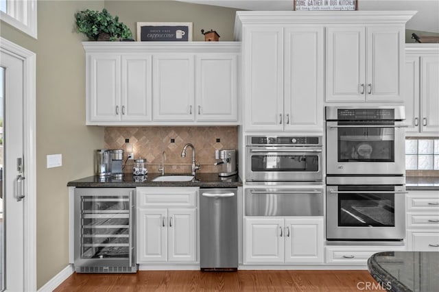 kitchen with beverage cooler, white cabinets, stainless steel double oven, a sink, and a warming drawer