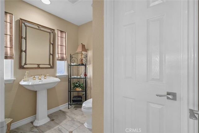 half bathroom featuring baseboards, a sink, and toilet