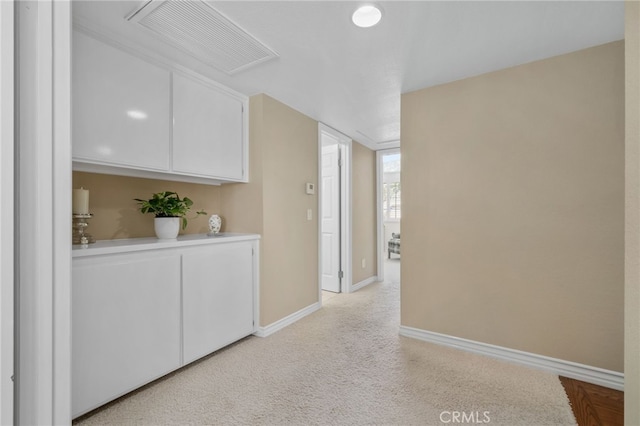 corridor with light carpet, visible vents, and baseboards