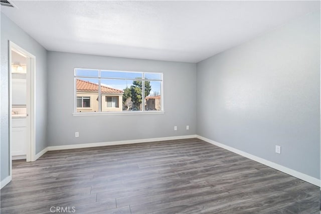 unfurnished room featuring dark wood-style floors, visible vents, and baseboards