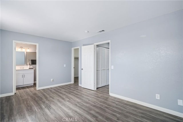 unfurnished bedroom with visible vents, ensuite bathroom, baseboards, and wood finished floors