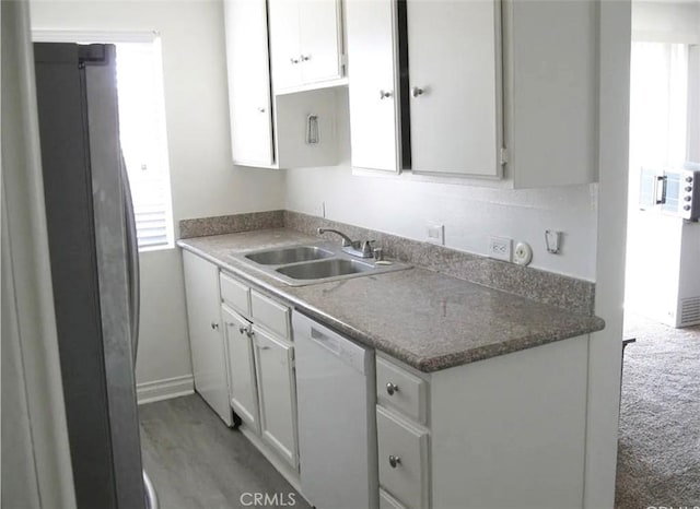 kitchen with dishwasher, dark countertops, a sink, and white cabinetry