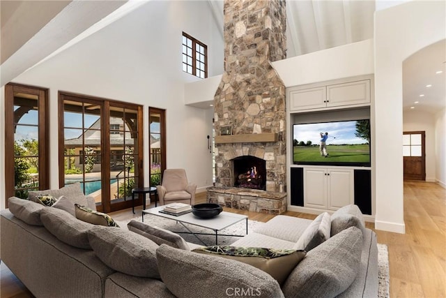 living room featuring light wood-type flooring, a fireplace, baseboards, and a high ceiling