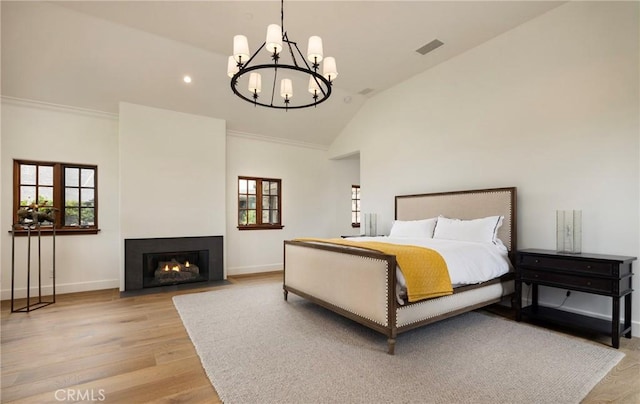 bedroom with lofted ceiling, a fireplace with flush hearth, visible vents, multiple windows, and light wood finished floors