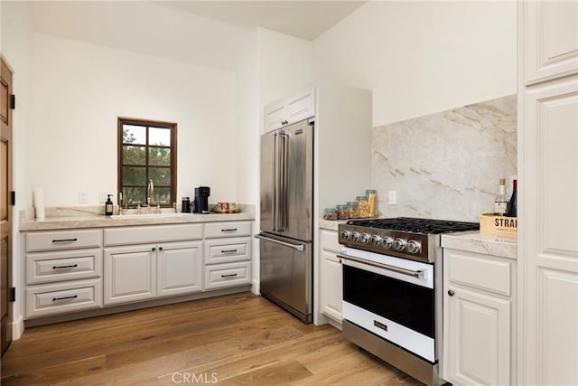 kitchen featuring tasteful backsplash, premium appliances, light wood-type flooring, white cabinetry, and a sink