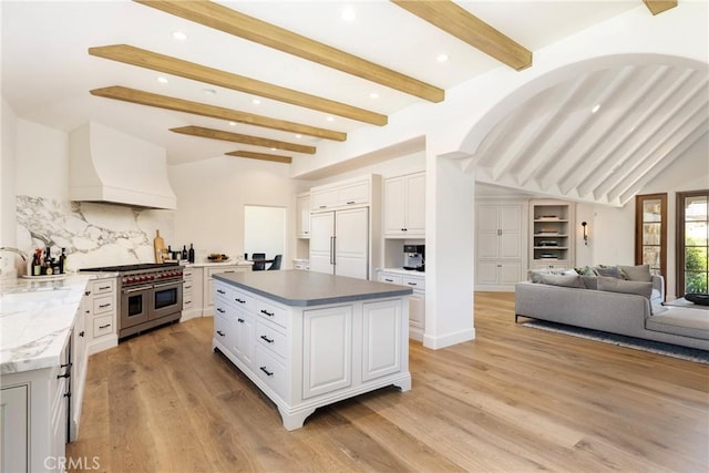 kitchen featuring premium appliances, a center island, custom range hood, open floor plan, and white cabinets