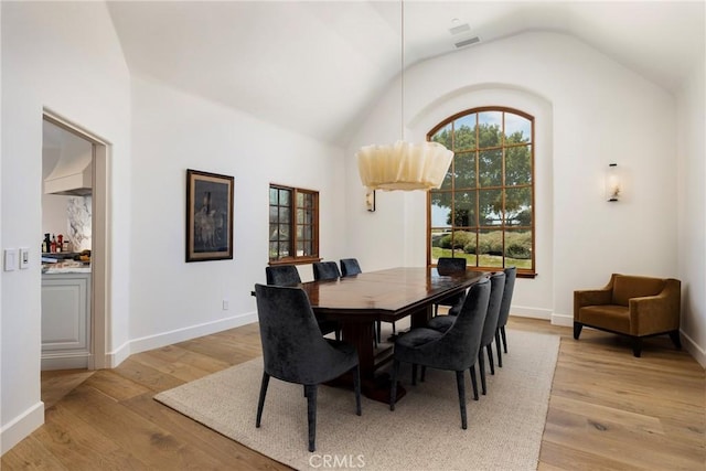 dining space with light wood-type flooring, visible vents, vaulted ceiling, and baseboards