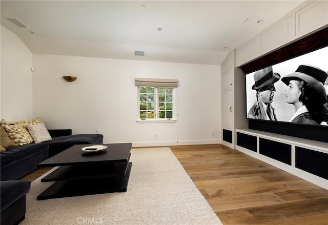 home theater with lofted ceiling, light wood finished floors, visible vents, and baseboards