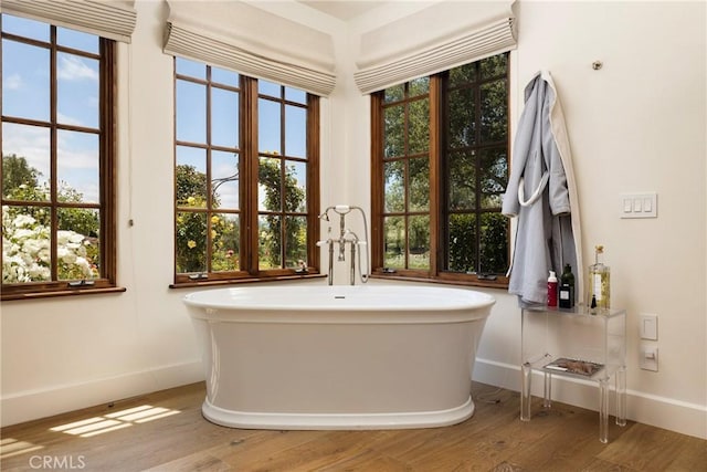 bathroom with a healthy amount of sunlight, a freestanding tub, and wood finished floors