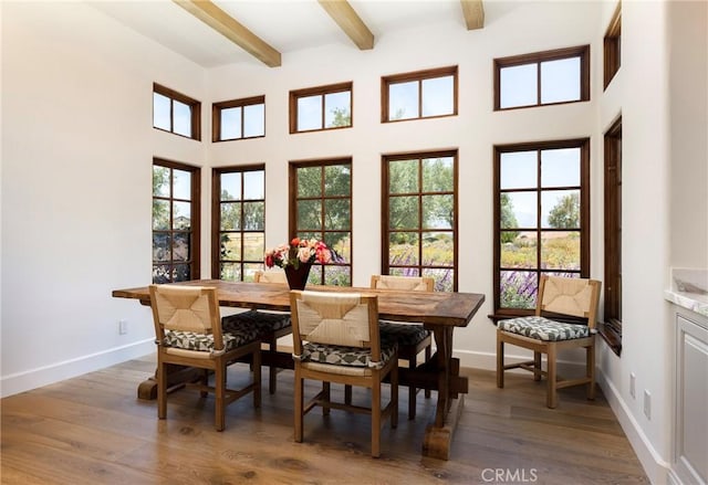 dining space featuring beamed ceiling, a towering ceiling, baseboards, and wood finished floors