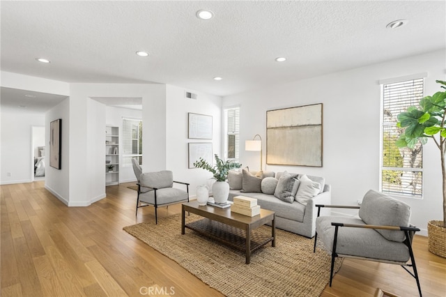 living room featuring a textured ceiling, light wood finished floors, visible vents, and recessed lighting