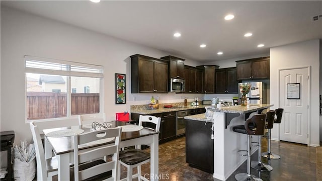 kitchen with stainless steel appliances, recessed lighting, dark brown cabinetry, and a breakfast bar area