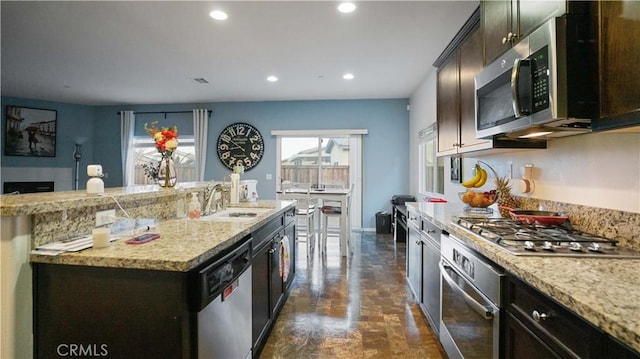 kitchen featuring recessed lighting, appliances with stainless steel finishes, a sink, an island with sink, and light stone countertops