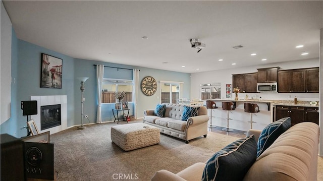 living room with recessed lighting, light colored carpet, visible vents, baseboards, and a glass covered fireplace