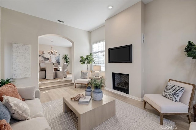 living area featuring arched walkways, a fireplace, visible vents, light wood-style flooring, and a chandelier