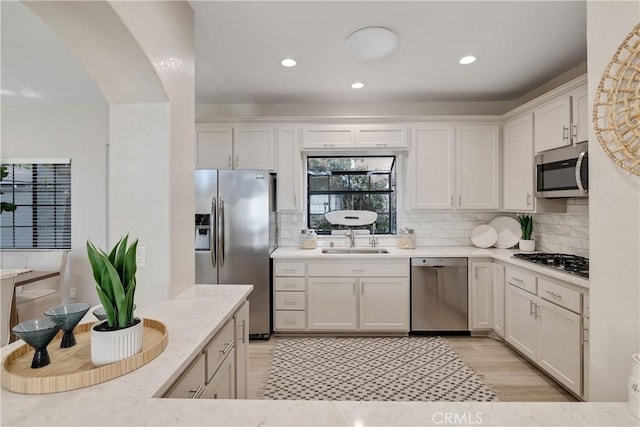 kitchen with arched walkways, decorative backsplash, white cabinets, appliances with stainless steel finishes, and a sink