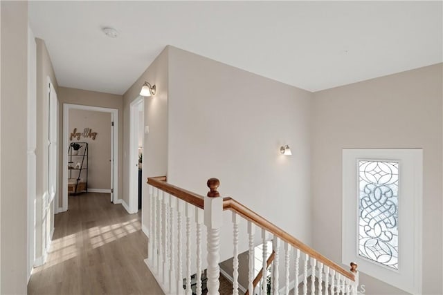 hallway featuring baseboards, wood finished floors, and an upstairs landing