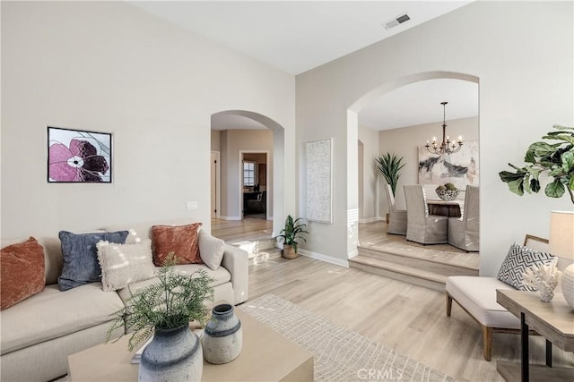 living room with arched walkways, light wood-style flooring, a notable chandelier, visible vents, and baseboards