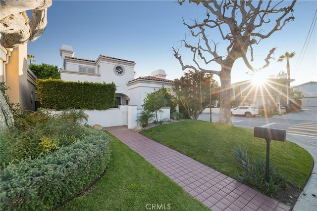 mediterranean / spanish-style house with a chimney, stucco siding, fence, a tiled roof, and a front lawn