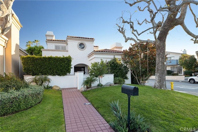 mediterranean / spanish-style house with a chimney, a front yard, and stucco siding