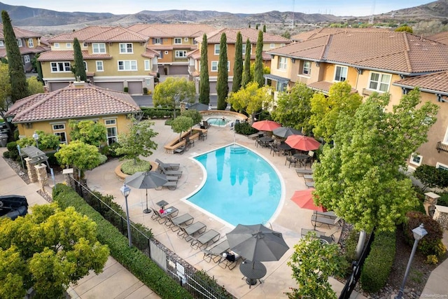 community pool with a residential view, a mountain view, fence, and a patio