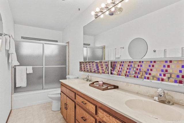 full bath featuring double vanity, bath / shower combo with glass door, a sink, and toilet