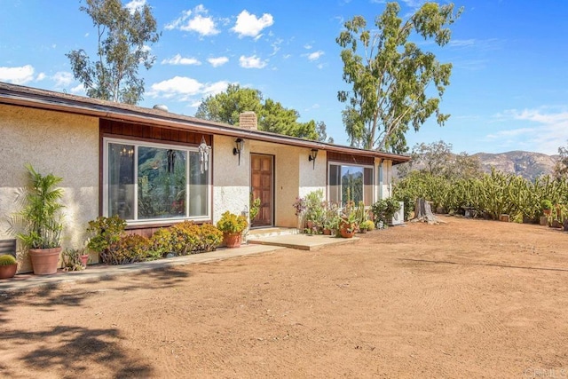 single story home featuring a chimney, a mountain view, and stucco siding