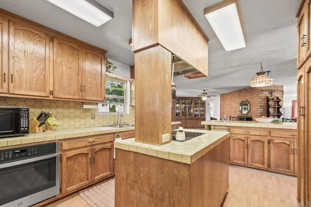 kitchen featuring a sink, a center island, black appliances, light wood finished floors, and tasteful backsplash