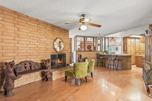 living area with a brick fireplace, a textured ceiling, and light wood finished floors