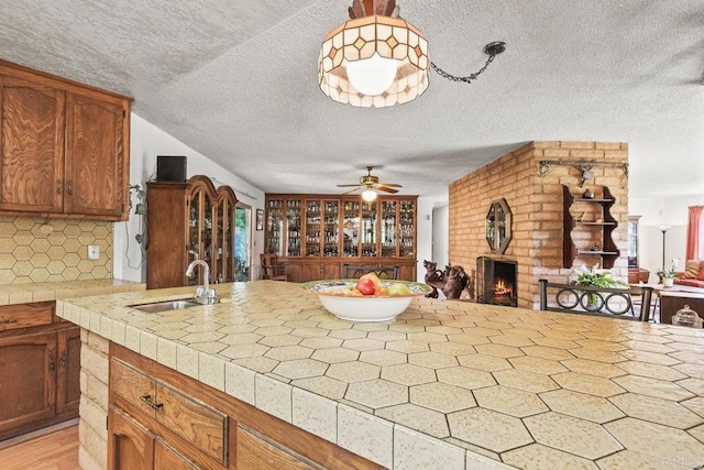 kitchen with a textured ceiling, a sink, open floor plan, a brick fireplace, and tasteful backsplash