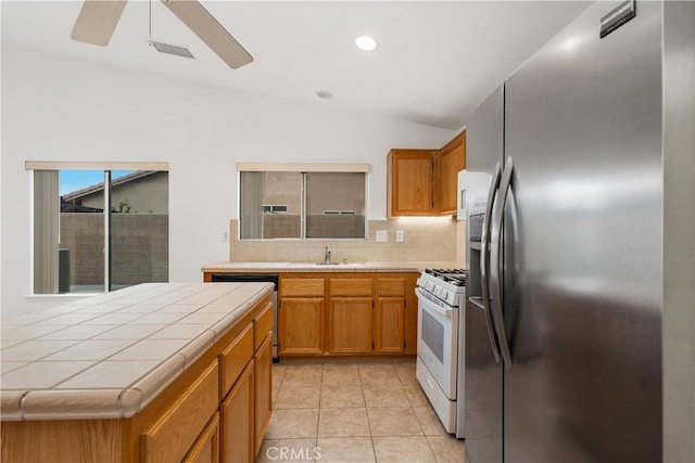 kitchen featuring decorative backsplash, tile countertops, stainless steel appliances, and lofted ceiling