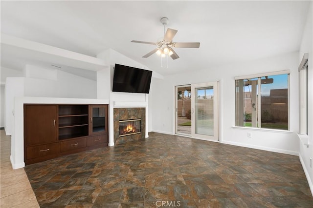 unfurnished living room featuring baseboards, vaulted ceiling, a glass covered fireplace, stone finish floor, and a ceiling fan