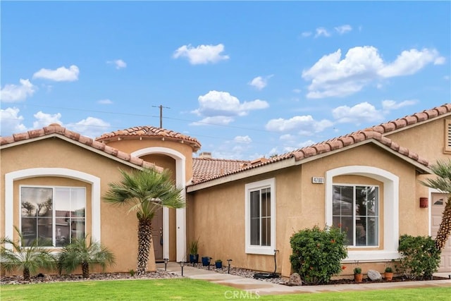 mediterranean / spanish house with a front lawn, a tiled roof, and stucco siding