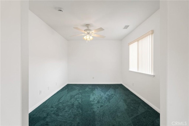 spare room with a ceiling fan, visible vents, dark colored carpet, and baseboards