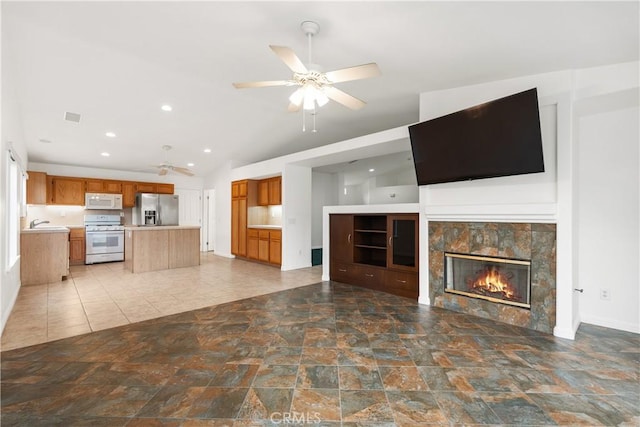 unfurnished living room featuring visible vents, a ceiling fan, a sink, a glass covered fireplace, and lofted ceiling