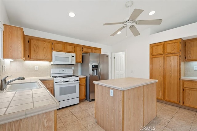 kitchen with a sink, white appliances, a center island, and tile counters