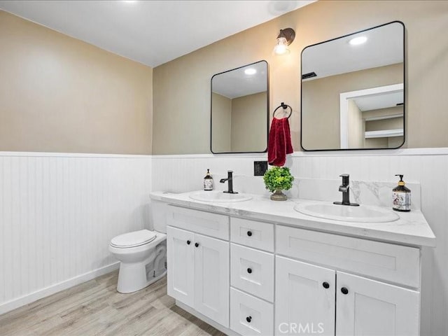 bathroom featuring a wainscoted wall, a sink, toilet, and wood finished floors