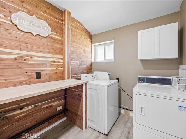 clothes washing area featuring wood walls, cabinet space, separate washer and dryer, and light wood-style floors