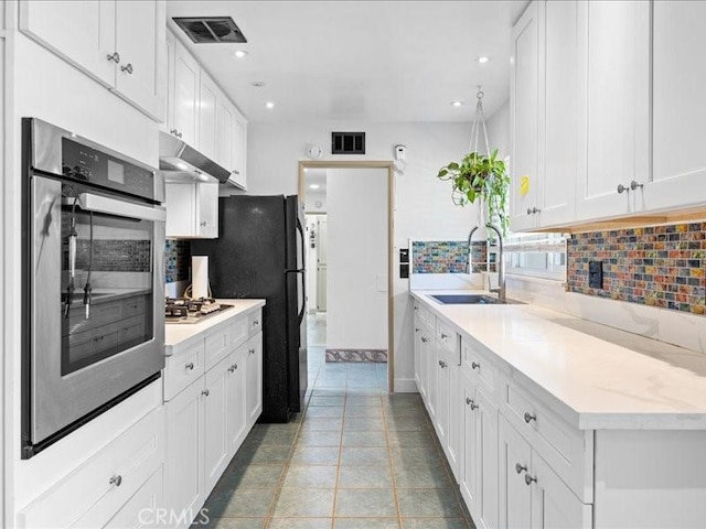 kitchen with under cabinet range hood, a sink, visible vents, light countertops, and decorative backsplash