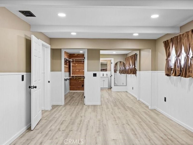empty room with a wainscoted wall, beam ceiling, visible vents, and light wood-style floors