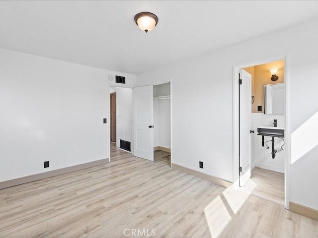 unfurnished bedroom with visible vents, light wood-style flooring, baseboards, and ensuite bathroom