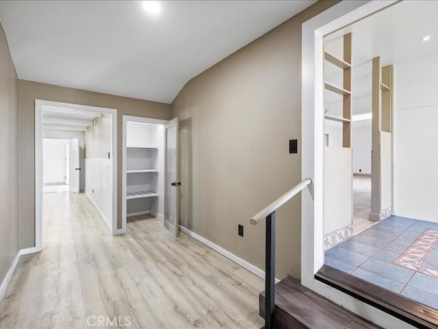 hall featuring light wood-type flooring, an upstairs landing, and baseboards