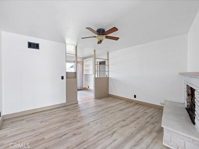 unfurnished living room featuring visible vents, ceiling fan, a stone fireplace, wood finished floors, and baseboards