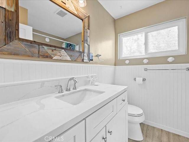full bath featuring a wainscoted wall, visible vents, toilet, vanity, and wood finished floors