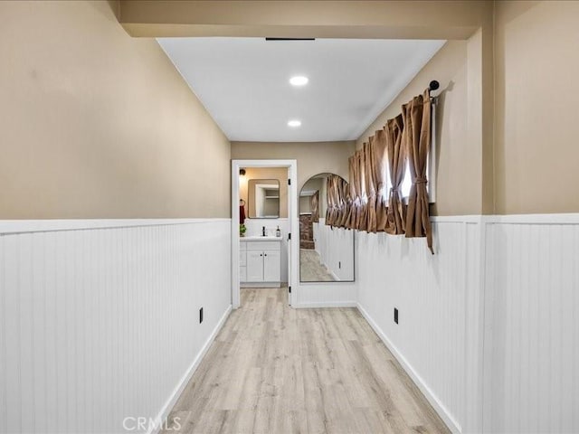 hall featuring arched walkways, light wood-type flooring, wainscoting, and a sink