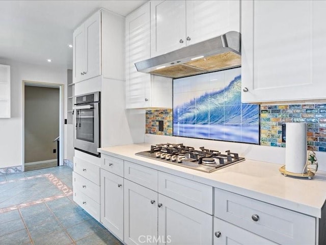 kitchen with under cabinet range hood, appliances with stainless steel finishes, white cabinets, and decorative backsplash