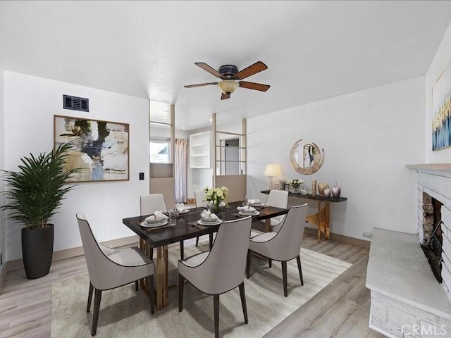 dining area featuring a fireplace with raised hearth, ceiling fan, visible vents, and light wood-style floors